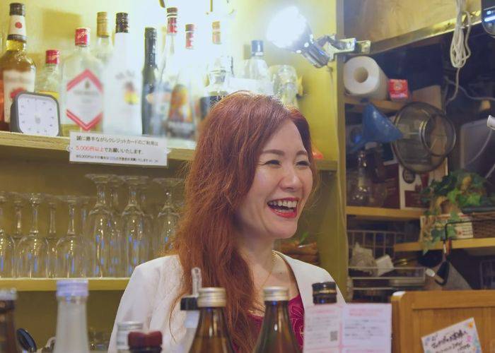 The host of a Tokyo snack bar, smiling at off-camera guests.